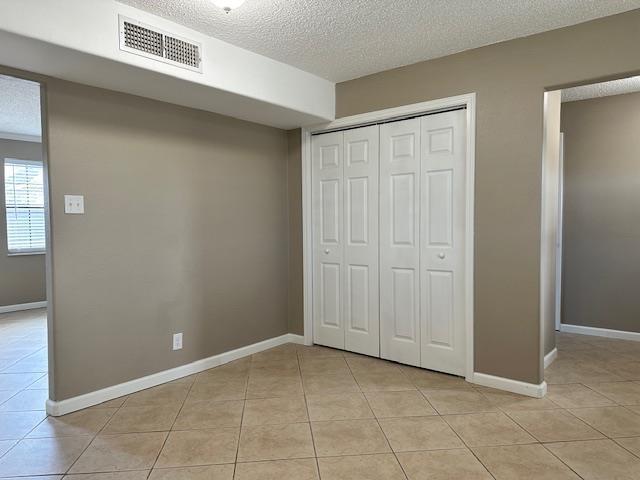 unfurnished bedroom featuring a textured ceiling, a closet, and light tile patterned flooring