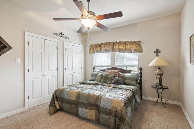 bedroom featuring ceiling fan, light colored carpet, and multiple closets