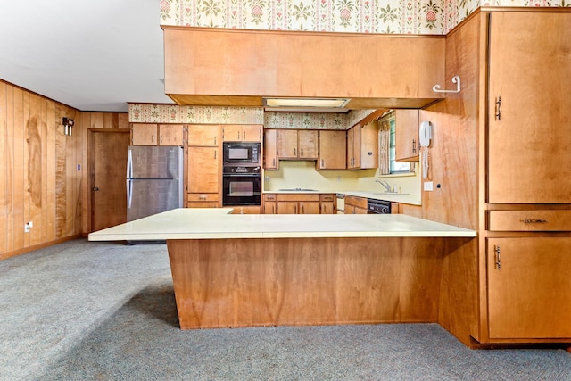 3030 Moore Rd, Beaumont, TX 77713 - kitchen featuring black appliances, carpet flooring, brown cabinets, light countertops, and wooden walls
