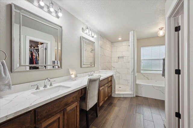 full bath with double vanity, a textured ceiling, tiled shower, and a sink