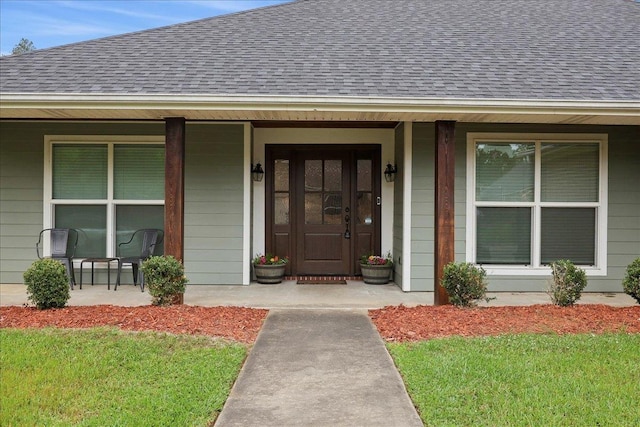 view of exterior entry featuring covered porch and roof with shingles