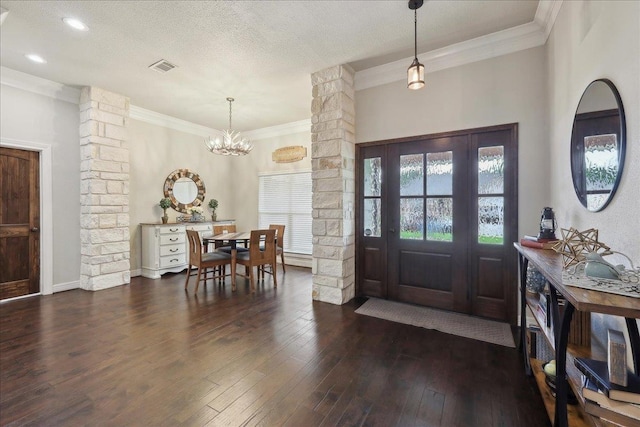entrance foyer featuring dark wood-style floors, visible vents, a notable chandelier, ornate columns, and ornamental molding