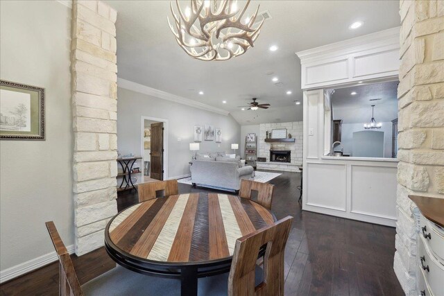 dining room with dark wood finished floors, baseboards, ceiling fan with notable chandelier, a fireplace, and ornamental molding