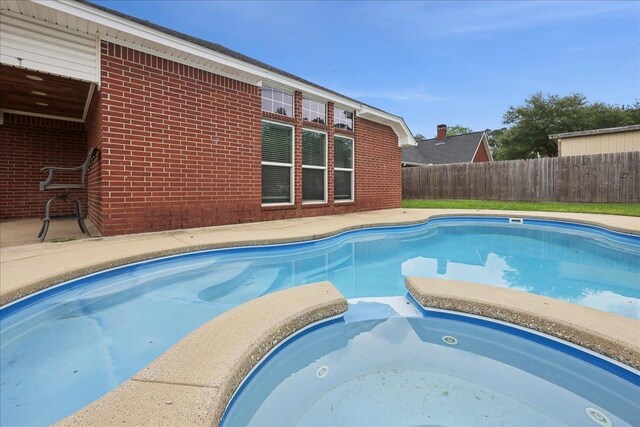 view of pool with fence and a pool with connected hot tub