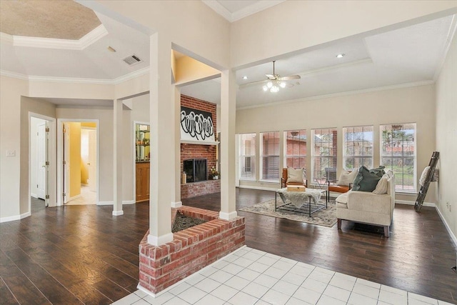 living room featuring wood-type flooring, ornamental molding, ceiling fan, a fireplace, and a tray ceiling