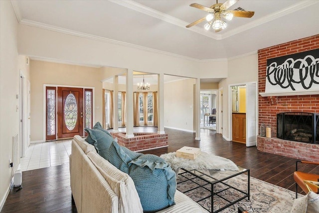 living room with ceiling fan with notable chandelier, a fireplace, ornamental molding, and wood-type flooring