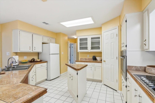 kitchen with appliances with stainless steel finishes, light tile patterned floors, a kitchen island, white cabinets, and sink