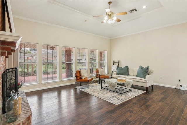 living room with ceiling fan, a brick fireplace, a tray ceiling, crown molding, and dark wood-type flooring