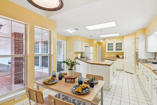 kitchen featuring white cabinets, stainless steel oven, white fridge, light tile patterned floors, and a skylight