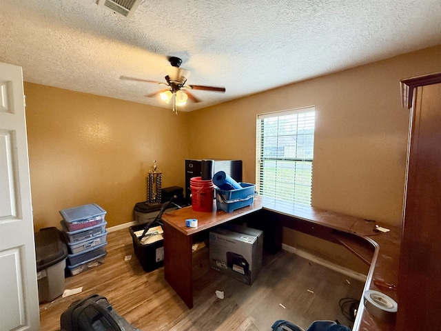 office with visible vents, a textured ceiling, wood finished floors, baseboards, and ceiling fan