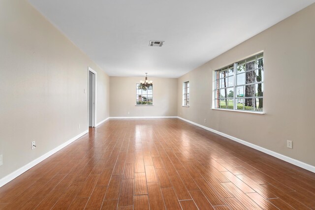 empty room with hardwood / wood-style floors and an inviting chandelier