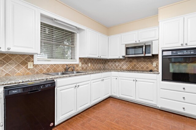 kitchen with backsplash, light stone counters, sink, black appliances, and white cabinetry