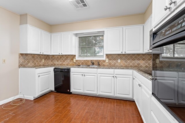 kitchen with dark stone countertops, white cabinetry, sink, and black dishwasher