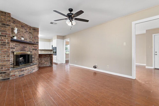 unfurnished living room with ceiling fan, wood-type flooring, and a brick fireplace