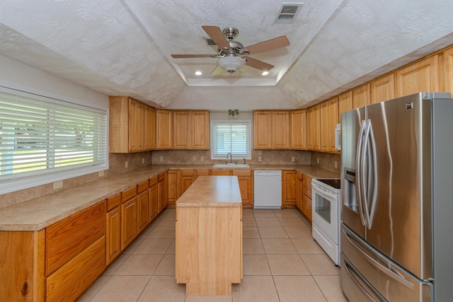 kitchen with white appliances, a raised ceiling, sink, a textured ceiling, and a kitchen island