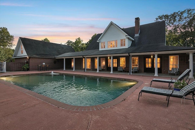 pool at dusk with pool water feature and a patio