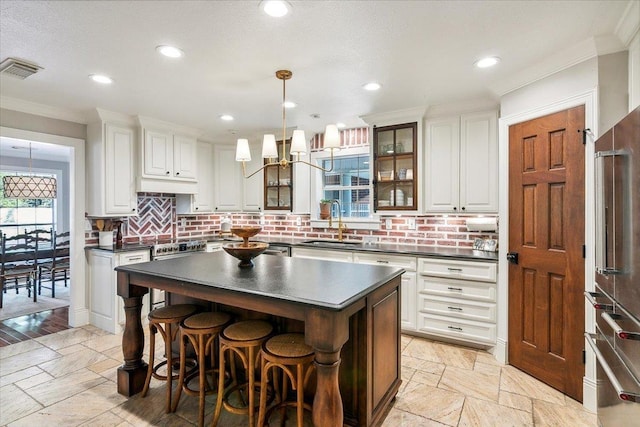 kitchen with white cabinetry, a center island, sink, tasteful backsplash, and decorative light fixtures