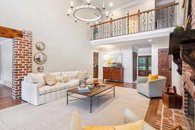 living room featuring a high ceiling, a brick fireplace, a notable chandelier, crown molding, and hardwood / wood-style floors