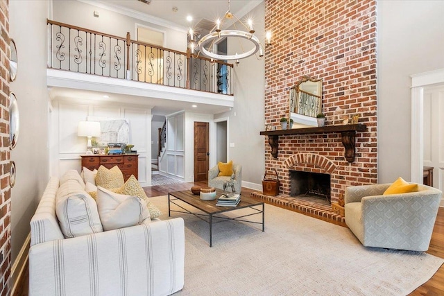 living room featuring a high ceiling, an inviting chandelier, a brick fireplace, wood-type flooring, and ornamental molding