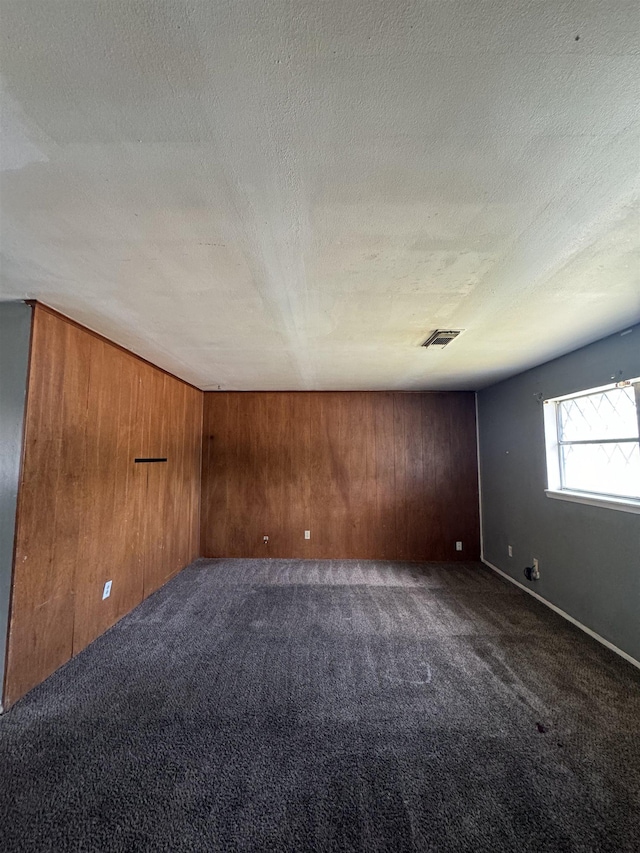 carpeted empty room with a textured ceiling and wooden walls