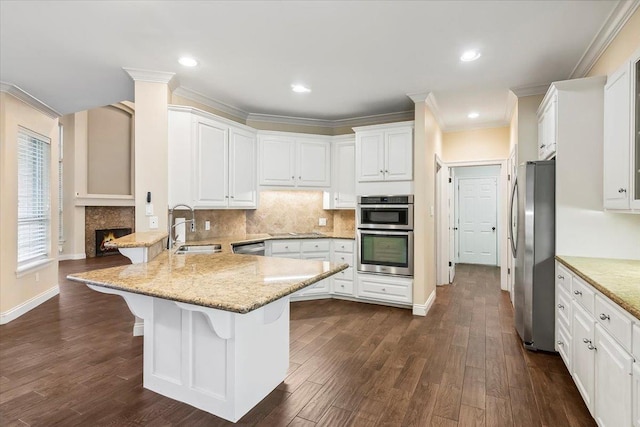 kitchen featuring a breakfast bar, sink, appliances with stainless steel finishes, light stone counters, and white cabinetry