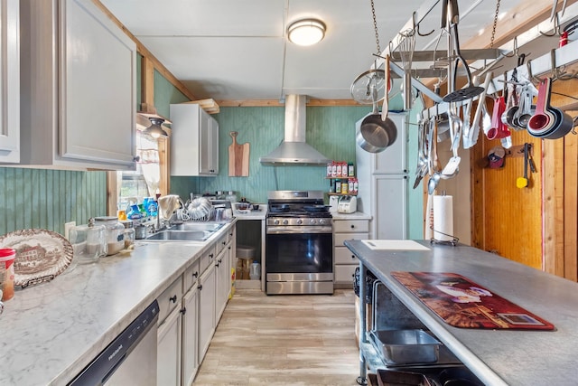 kitchen with sink, wall chimney range hood, appliances with stainless steel finishes, white cabinets, and light wood-type flooring