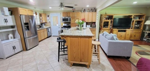 kitchen with a kitchen breakfast bar, ceiling fan, ornamental molding, a kitchen island, and stainless steel appliances