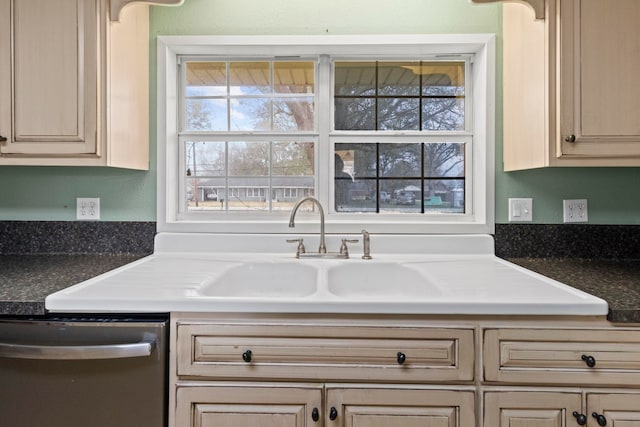 kitchen featuring a sink, stainless steel dishwasher, dark countertops, and cream cabinets