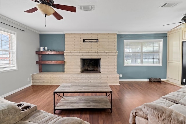 living area with visible vents, wood finished floors, a fireplace, and crown molding