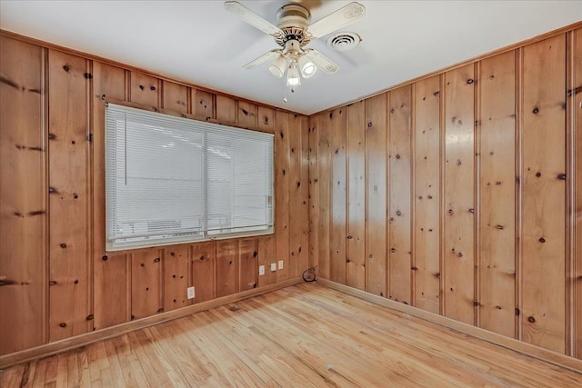 empty room with light hardwood / wood-style flooring, wooden walls, and ceiling fan