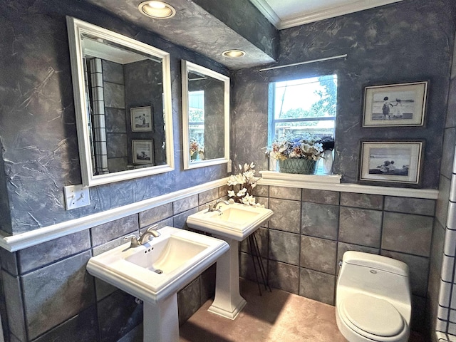 bathroom with toilet, dual sinks, crown molding, and tile walls