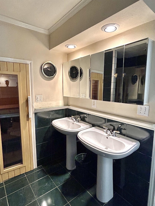 bathroom featuring tile patterned flooring, dual sinks, crown molding, and tile walls