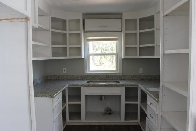 kitchen with stone countertops, white cabinetry, sink, and a wall mounted AC