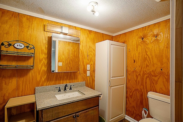 bathroom featuring vanity, wood walls, toilet, ornamental molding, and a textured ceiling