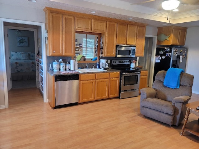 kitchen featuring appliances with stainless steel finishes, ornamental molding, a raised ceiling, sink, and light hardwood / wood-style floors