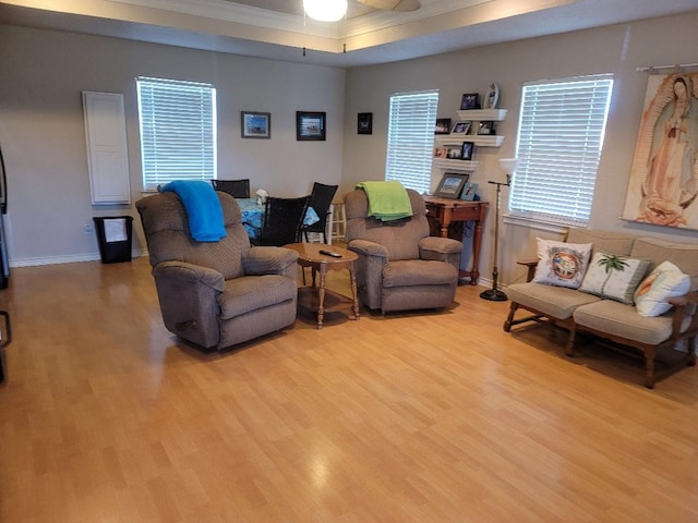 living room with light wood-type flooring, a tray ceiling, ceiling fan, and ornamental molding