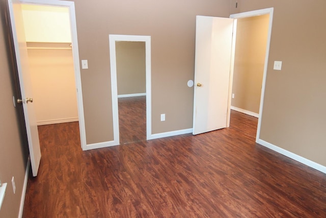 unfurnished bedroom featuring a walk in closet, a closet, and dark hardwood / wood-style flooring