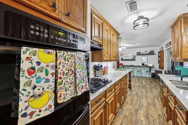 1407 N 15th St, Nederland, TX 77627 - kitchen with black appliances, light wood-style flooring, brown cabinetry, light stone countertops, and a sink