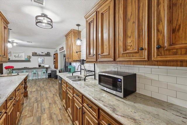 1407 N 15th St, Nederland, TX 77627 - kitchen featuring appliances with stainless steel finishes, brown cabinetry, a textured ceiling, a sink, and backsplash