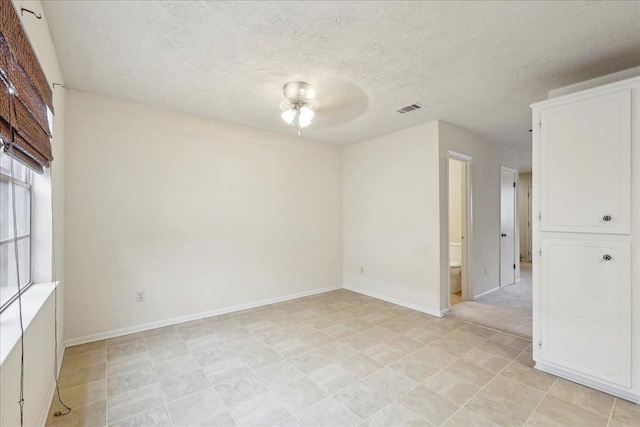 spare room featuring baseboards, visible vents, a textured ceiling, and a ceiling fan