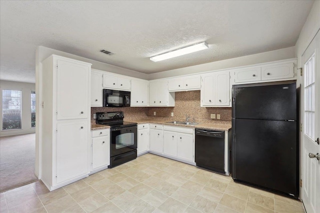 kitchen with black appliances, white cabinets, visible vents, and a sink