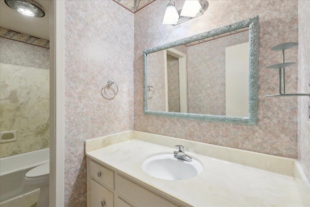 bathroom with toilet, wallpapered walls, and vanity