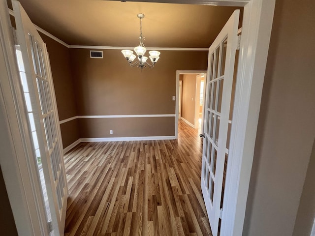 unfurnished dining area featuring french doors, wood-type flooring, ornamental molding, and a notable chandelier