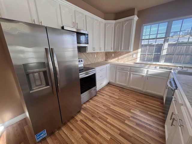 kitchen with white cabinets, tasteful backsplash, light wood-type flooring, and appliances with stainless steel finishes