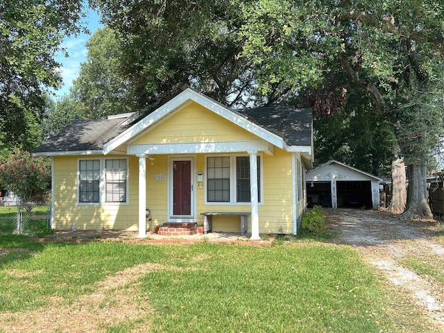 bungalow-style home with covered porch, an outbuilding, a garage, and a front lawn