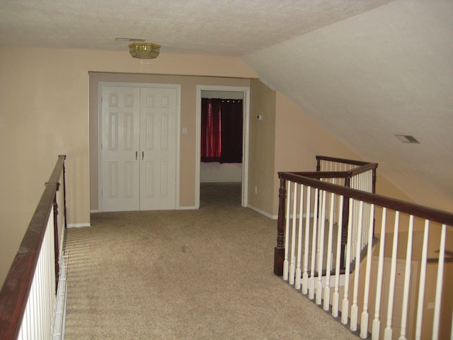 hallway with a textured ceiling, light colored carpet, and lofted ceiling