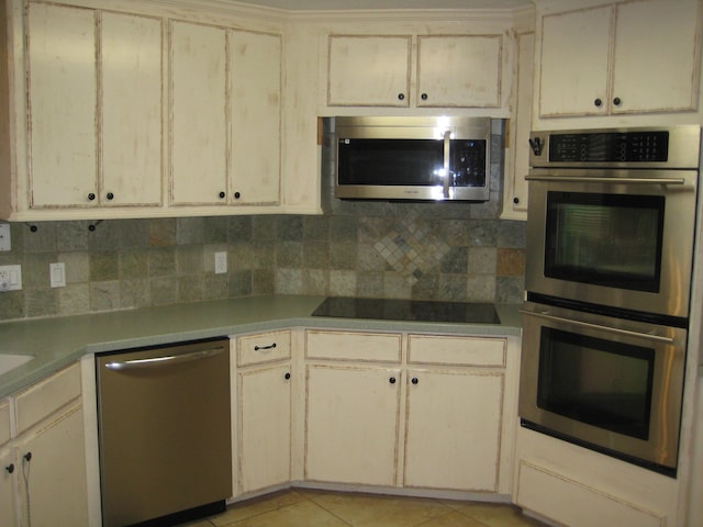 kitchen with backsplash, cream cabinets, light tile patterned flooring, and appliances with stainless steel finishes