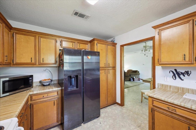 kitchen featuring a textured ceiling, light countertops, visible vents, brown cabinetry, and appliances with stainless steel finishes