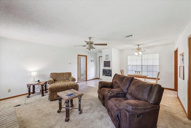 living area with visible vents, baseboards, a ceiling fan, a textured ceiling, and light colored carpet
