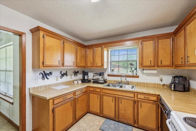 kitchen with electric range, a textured ceiling, light countertops, a sink, and brown cabinets
